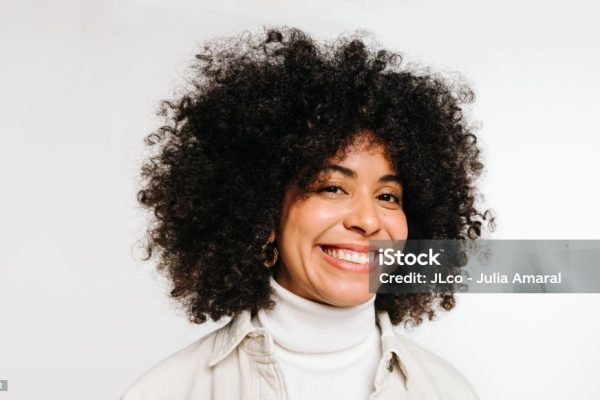 Portrait of a happy woman with curly hair smiling at the camera while standing against a white background. Beautiful young woman of colour wearing her natural hair with pride.